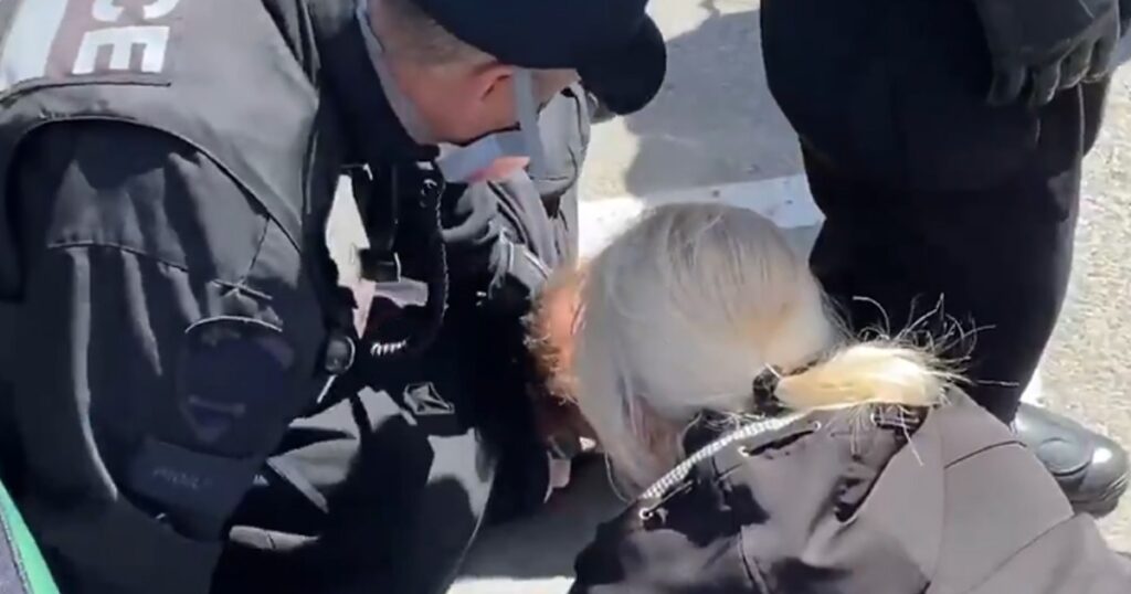 Video recorded by Rebel News reporter Mocha Bezirgan shows a police officer in Montreal, Canada choke a man who was laying on the ground in the process of an arrest for not wearing a face mask outside and in public. The man, who had already been tackled on the ground by police and was in the process of being subdued by a crowd of regular police and riot control police during a lockdown protest in Montreal, Canada, began shouting at the officers. Seconds later, a riot police officer used his left hand to restrain and choke the man by his neck, prompting members of the crowd to begin shouting. Police officers then attempted to block the cameras recording the scene.
