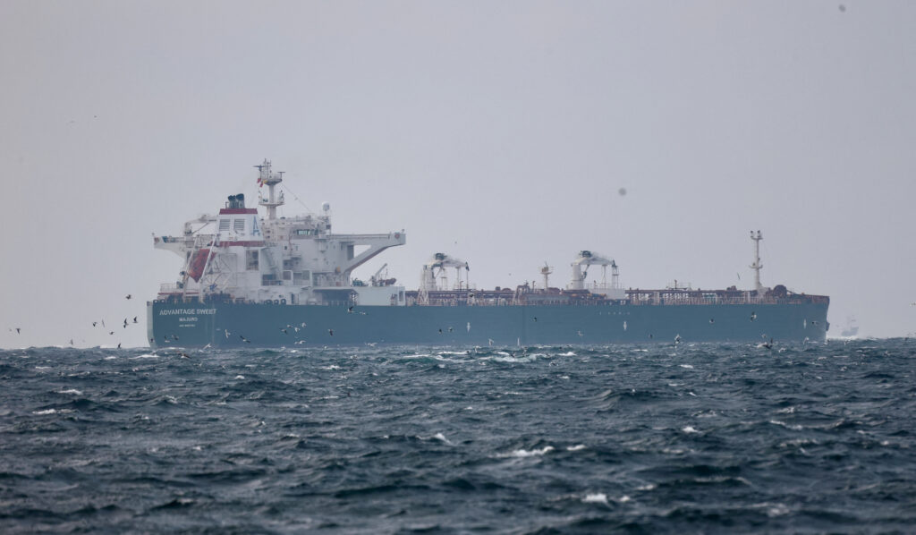 Large oil tanker sailing on open ocean waters while being monitored by a nearby naval vessel, symbolizing a maritime seizure operation.