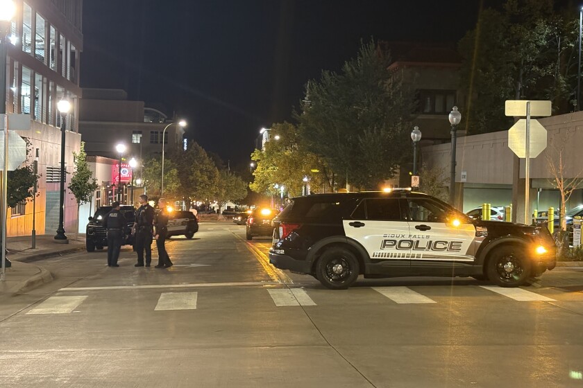 Police officers patrol a quiet downtown American street with a city skyline visible during daytime, reflecting reduced crime and increased law enforcement presence.