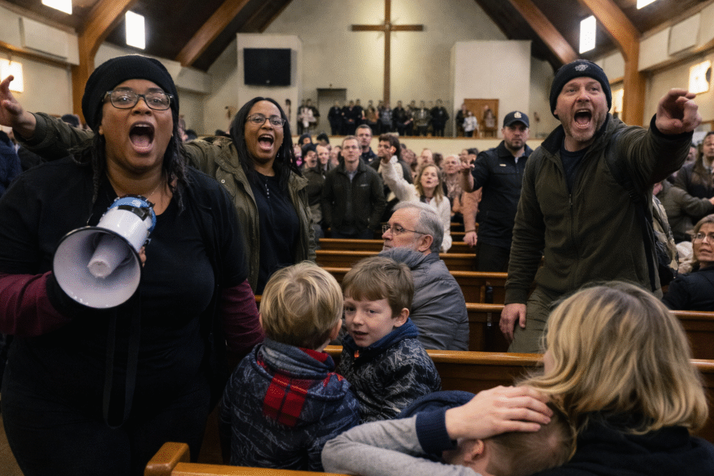 Protesters confront congregants inside a church sanctuary during a worship service, shouting and holding a megaphone as families and children sit distressed in the pews beneath a cross at the front of the church.