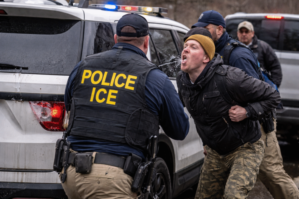 Man identified as Alex Pretti confronts ICE agents beside a federal vehicle, appearing to spit at an officer while other agents intervene during a street encounter.