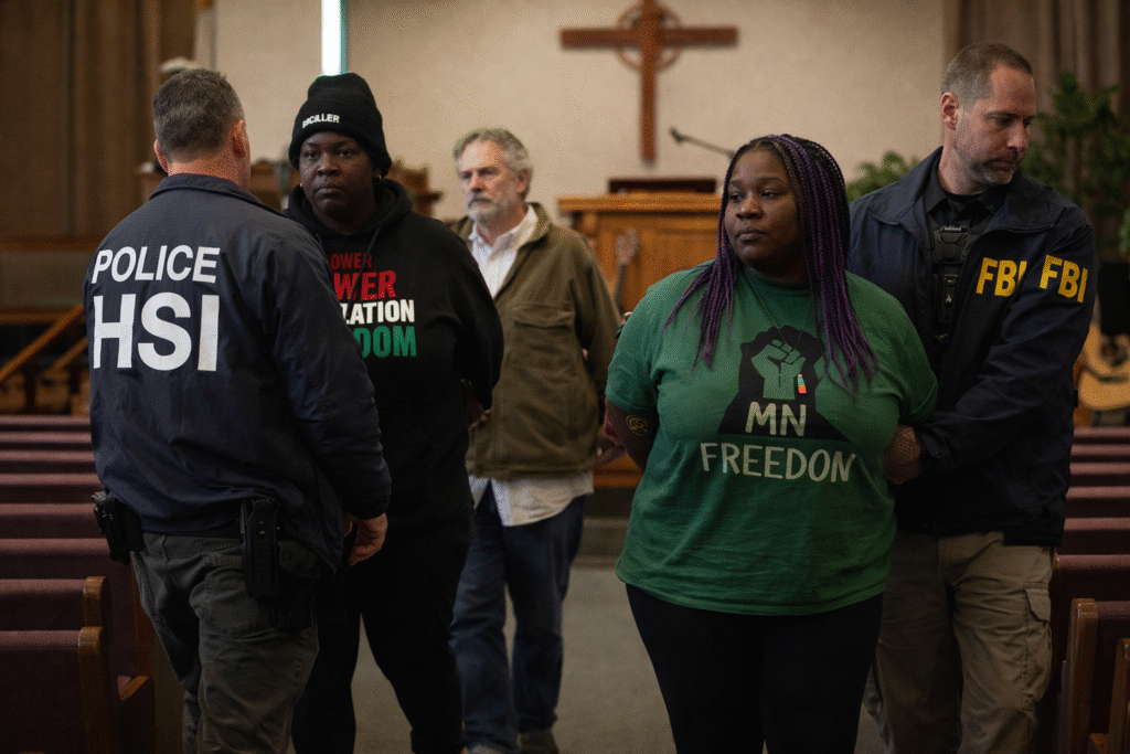 Law enforcement officers escort three protesters out of a Minnesota church sanctuary, with wooden pews and a cross visible in the background during a daytime arrest scene.