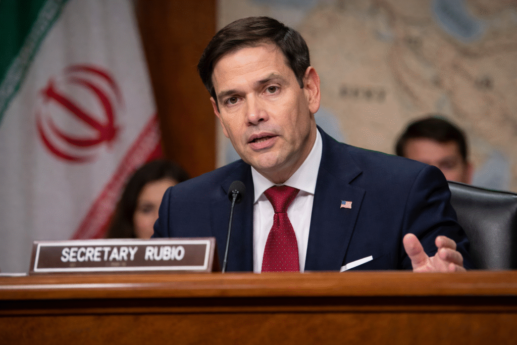 U.S. Secretary of State Marco Rubio testifies before the Senate Foreign Relations Committee during a hearing on Iran, with the Iranian flag visible in the background.