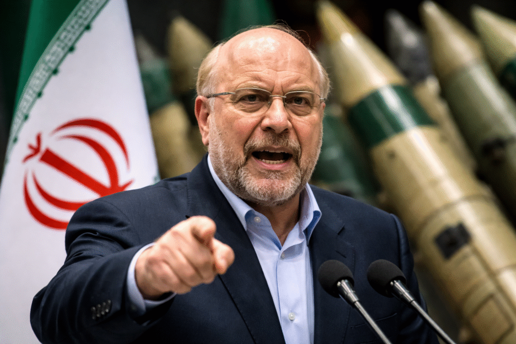 Iranian parliamentary speaker Mohammad Bagher Ghalibaf speaks at a podium with the Iranian flag visible behind him and missile imagery in the background.