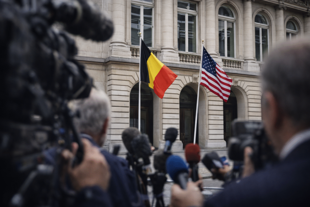 Belgium Foreign Ministry building in Brussels with Belgian and U.S. flags and blurred press equipment in foreground, symbolizing a diplomatic dispute over antisemitism claims.