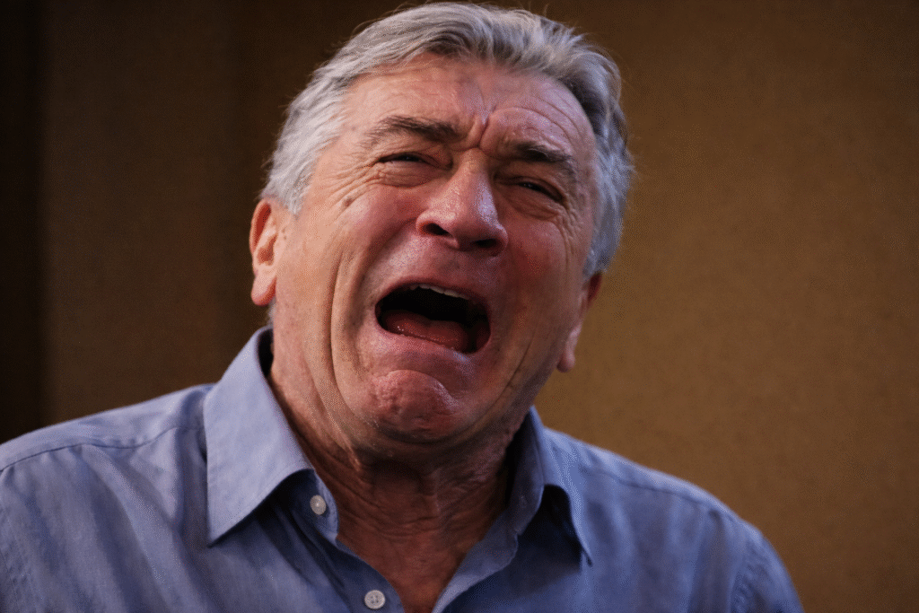 Close-up of Robert De Niro with an anguished expression, mouth open and eyes teary, against a softly blurred background.