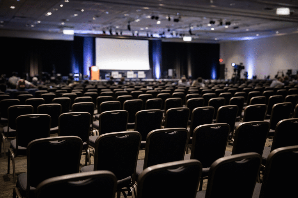 Empty conference hall with rows of chairs and a stage in the background, illustrating a large professional event setting.