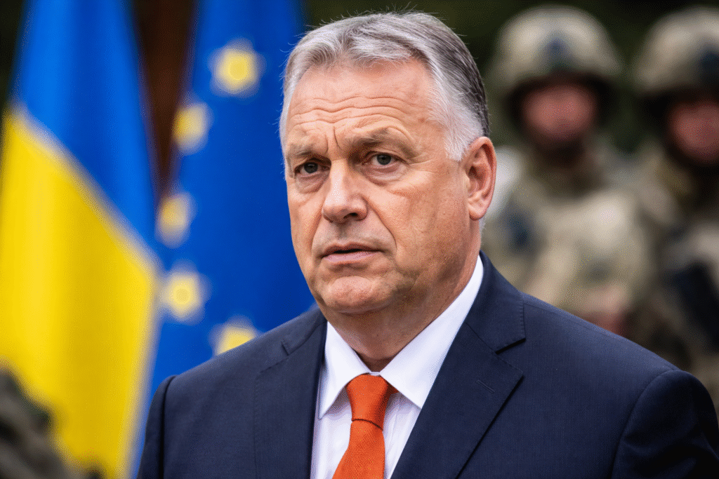 Hungarian Prime Minister Viktor Orban speaking in front of blurred EU and Ukrainian flags with soldiers in the background