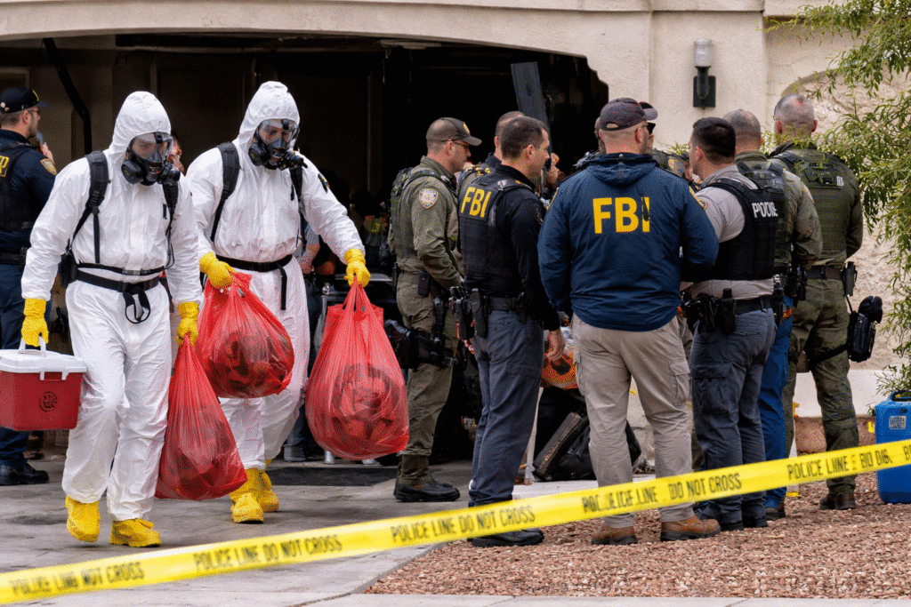 Hazmat-suited personnel and FBI agents stand outside a Las Vegas home as authorities remove materials during an investigation into a suspected residential biolab, with police tape securing the scene.