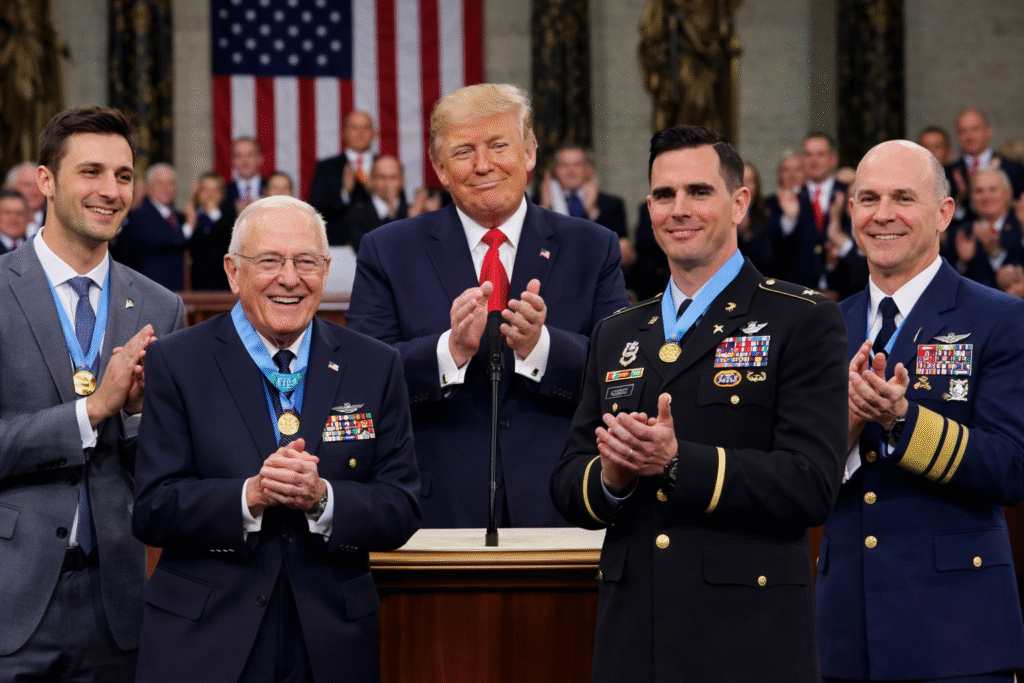 President Donald Trump applauding beside U.S. military honorees wearing formal uniforms and medals during a State of the Union ceremony inside the Capitol.