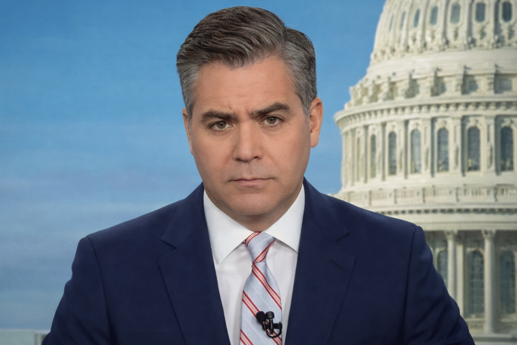 Close-up of journalist Jim Acosta wearing a navy suit and striped tie, seated in a studio setting with the U.S. Capitol dome visible in the background.