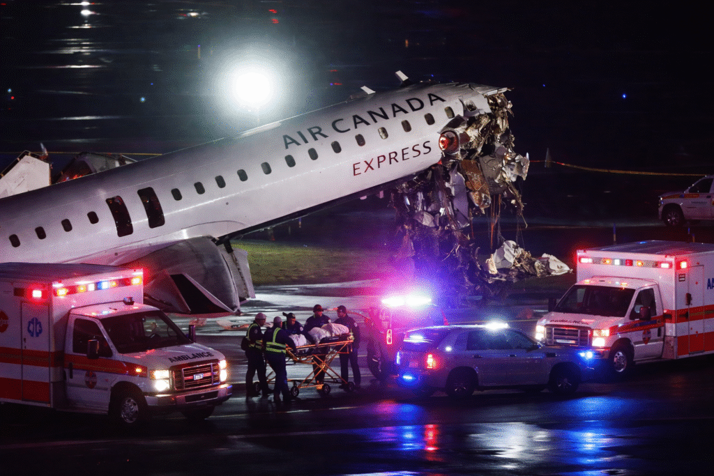 Emergency responders and medical personnel attend to a damaged Air Canada aircraft on a runway at night, with ambulances and flashing lights surrounding the crash site at an airport.