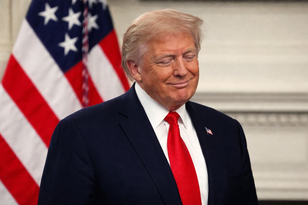 Donald Trump with eyes closed and a slight smile, wearing a dark suit and red tie, standing in front of an American flag in a calm, reflective moment.