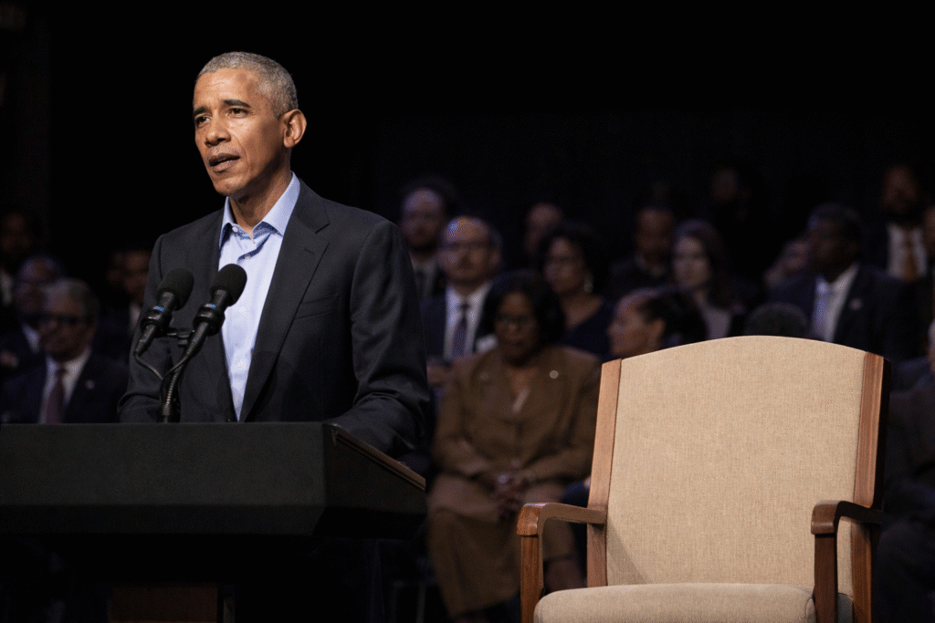 Former president speaking at a formal public event while standing on stage with an audience and empty seating nearby.