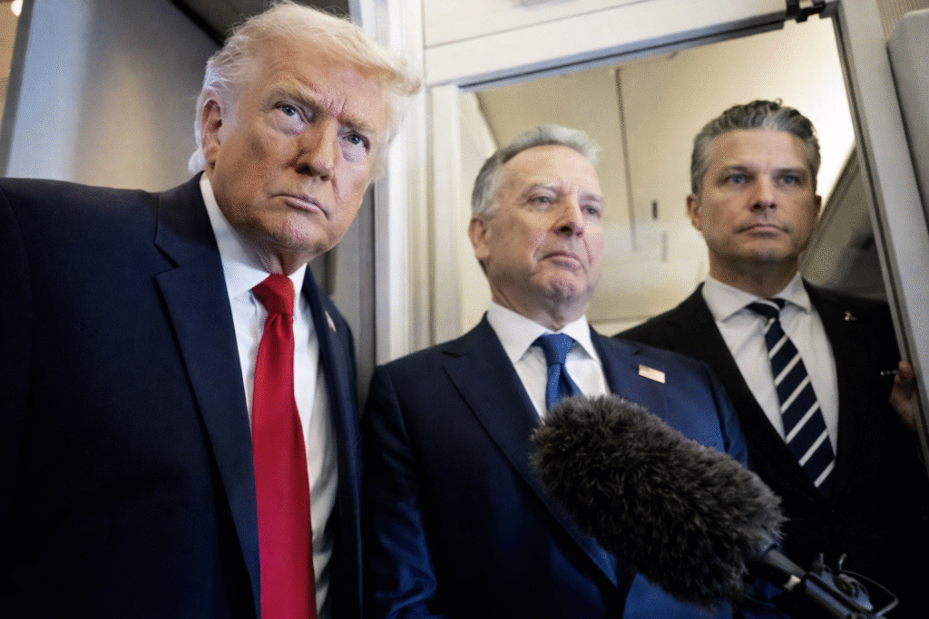 Former President Donald Trump speaking with reporters inside an aircraft doorway while two officials stand beside him as a microphone is held toward them.
