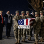 U.S. military honor guard carrying a flag-draped transfer case during a dignified transfer ceremony at Dover Air Force Base as officials salute the fallen service members.