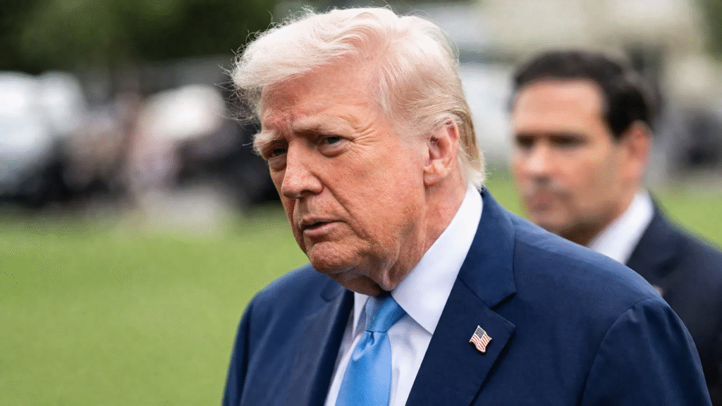 Close-up of Donald Trump outdoors wearing a suit and tie, with a blurred background and another person standing behind him.