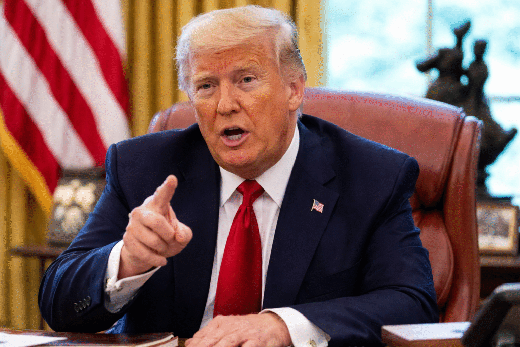 President Donald Trump speaking from behind a desk in the Oval Office while pointing forward, with the American flag visible in the background.