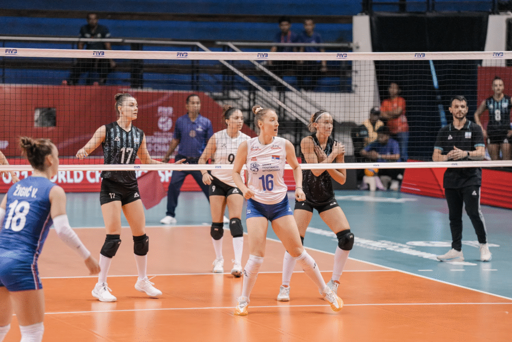 Women’s volleyball teams competing during an indoor match, with players positioned near the net preparing for the next play on a professional court.
