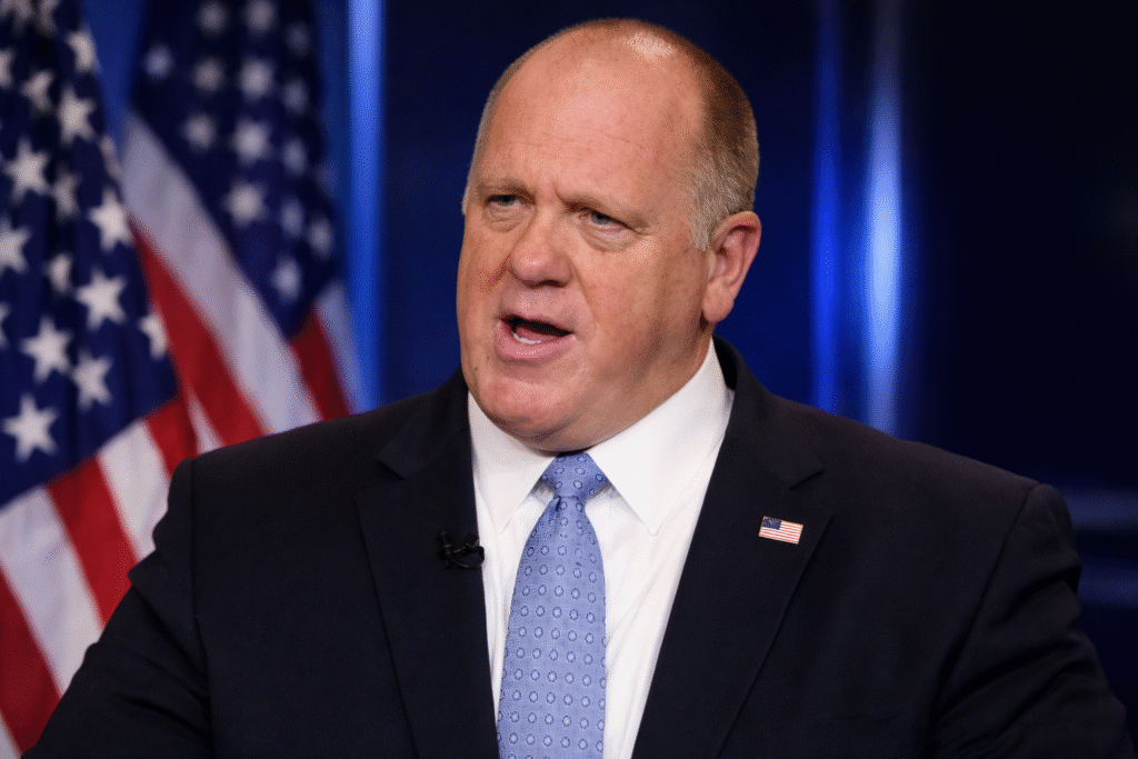 Tom Homan speaking during a televised interview with an American flag behind him, representing discussion on the DHS shutdown and immigration policy debate.