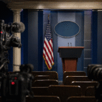 Empty press briefing room with podium and cameras representing political tension and media speculation