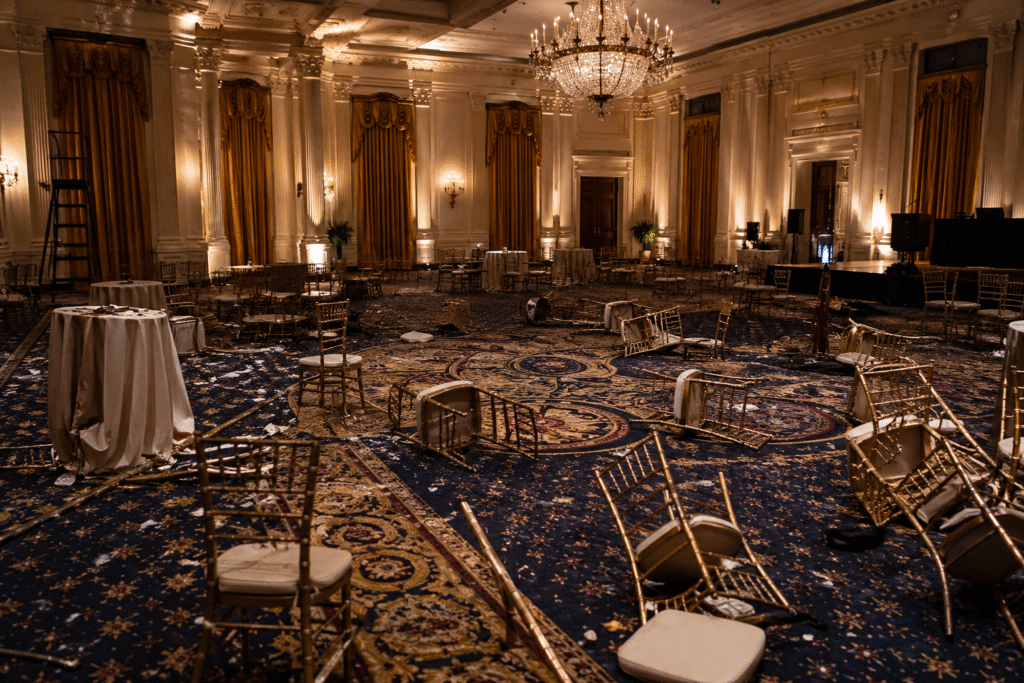Empty formal ballroom with scattered chairs and subdued lighting, suggesting disruption after a high-profile event.