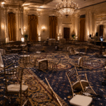 Empty formal ballroom with scattered chairs and subdued lighting, suggesting disruption after a high-profile event.