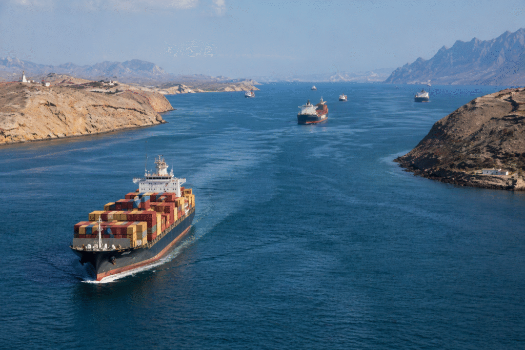Cargo ships navigating a narrow maritime strait between coastlines, representing global shipping routes and geopolitical tensions in the Bab al-Mandeb region.