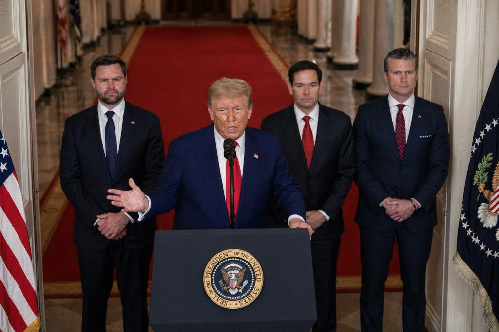 Man at a presidential podium gesturing with one hand while speaking, with three suited officials standing behind him in a formal government hallway lined with columns and a red carpet.
