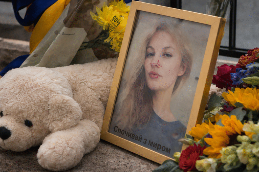 Memorial display featuring a framed portrait of a young woman surrounded by flowers and a plush teddy bear, arranged outdoors in remembrance.