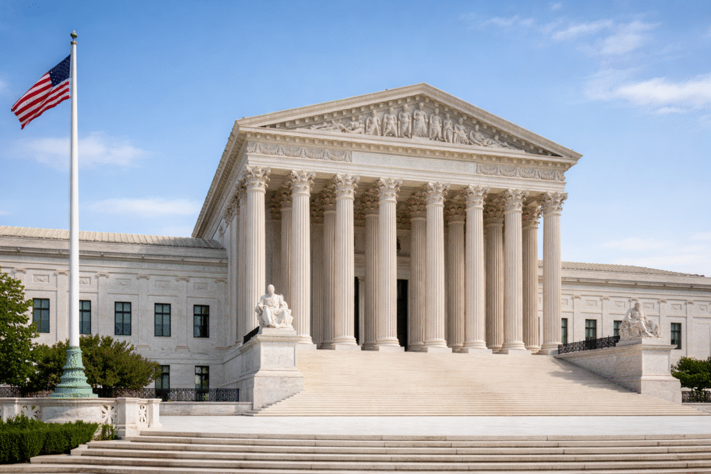 Exterior view of the United States Supreme Court building with large columns, steps, and an American flag under a clear sky.