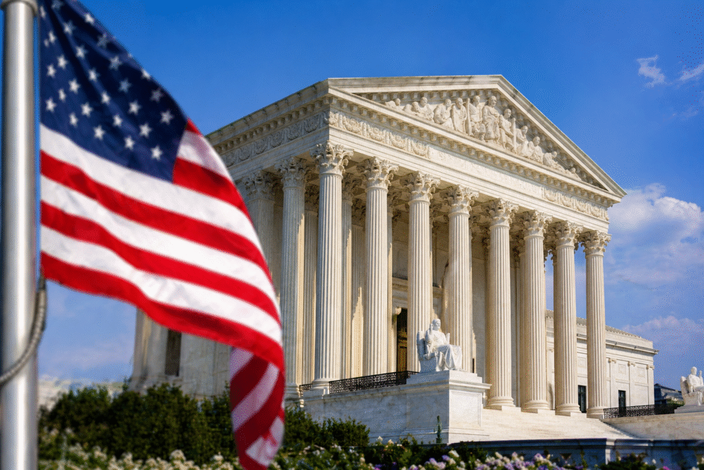 Neoclassical courthouse building with tall columns under a clear blue sky, with an American flag prominently displayed in the foreground.