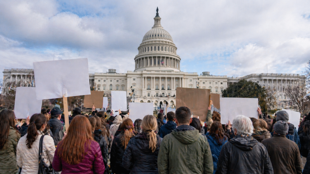 Large crowd gathered in front of the U.S. Capitol building holding blank signs during a peaceful demonstration related to government policy and funding