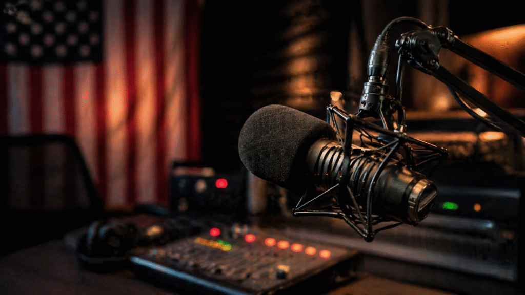 Close-up of a professional broadcast microphone in a dimly lit studio with blurred American flag and audio equipment in the background