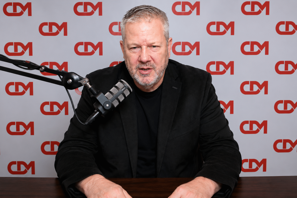 L Todd Wood speaking into a studio microphone during a podcast-style interview in front of a repeating CDM backdrop.